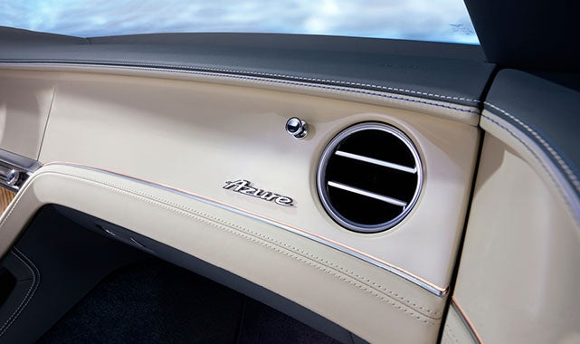 Close-up of dashboard showcasing soft-touch cream leather, contrast stitching, and an elegant Azure nameplate beside the circular air vent.