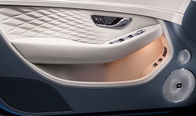 Interior door panel highlighting quilted leather, chrome trim, ambient lighting, and precision-crafted audio speaker grilles.