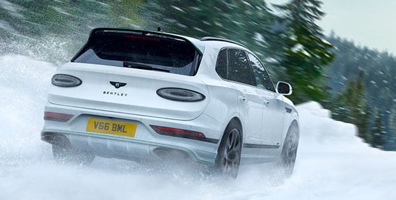 Rear view of the 2026 Bentley Bentayga Speed in motion on a snowy mountain road, emphasizing its confident all-wheel drive and winter handling.