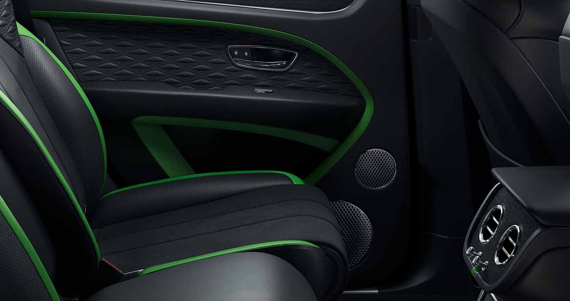 Rear passenger seat and door trim of the 2026 Bentley Bentayga Speed, featuring diamond-stitched leather, green accents, and integrated speaker grilles.