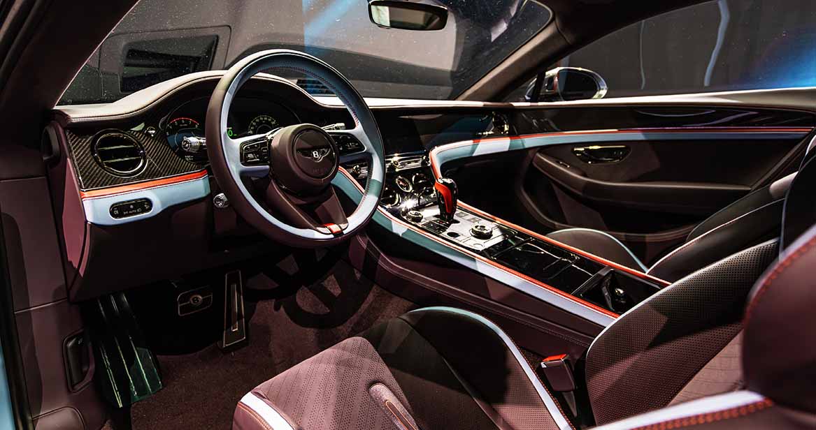2026 Bentley Supersports cockpit interior showing a carbon fiber dashboard, contrast red and light blue trim, digital display cluster, and leather-wrapped flat-bottom steering wheel.
