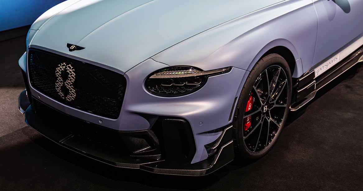 Front angle of a Bentley Continental GT Supersports featuring blacked-out grille with Bentley 'B' emblem, matte paint finish, and striking red brake calipers behind gloss black alloy wheels.