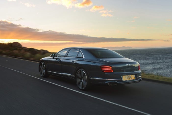 Rear view of a 2027 Bentley Flying Spur driving along the coast at sunset