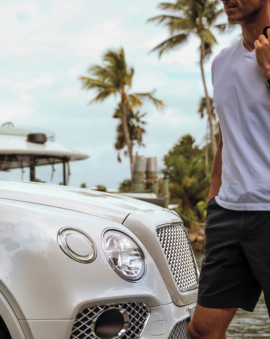 Man walking in front of Bentley with palm trees in the background