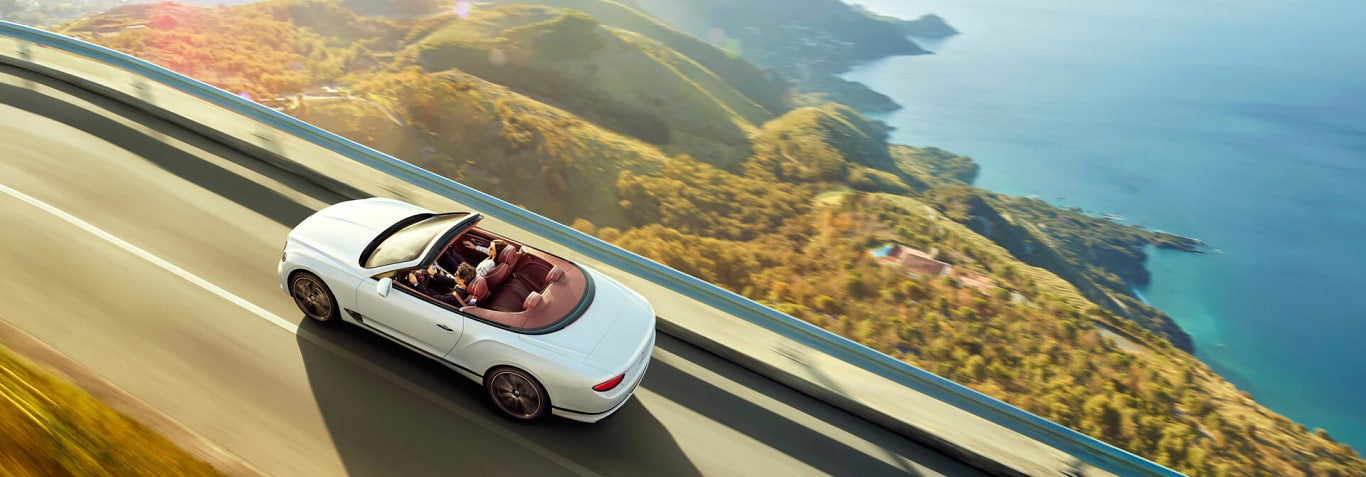 new white Bentley Continental GT Convertible driving on high mountain road with sea to the right | Bentley Tampa Bay in Pinellas Park FL